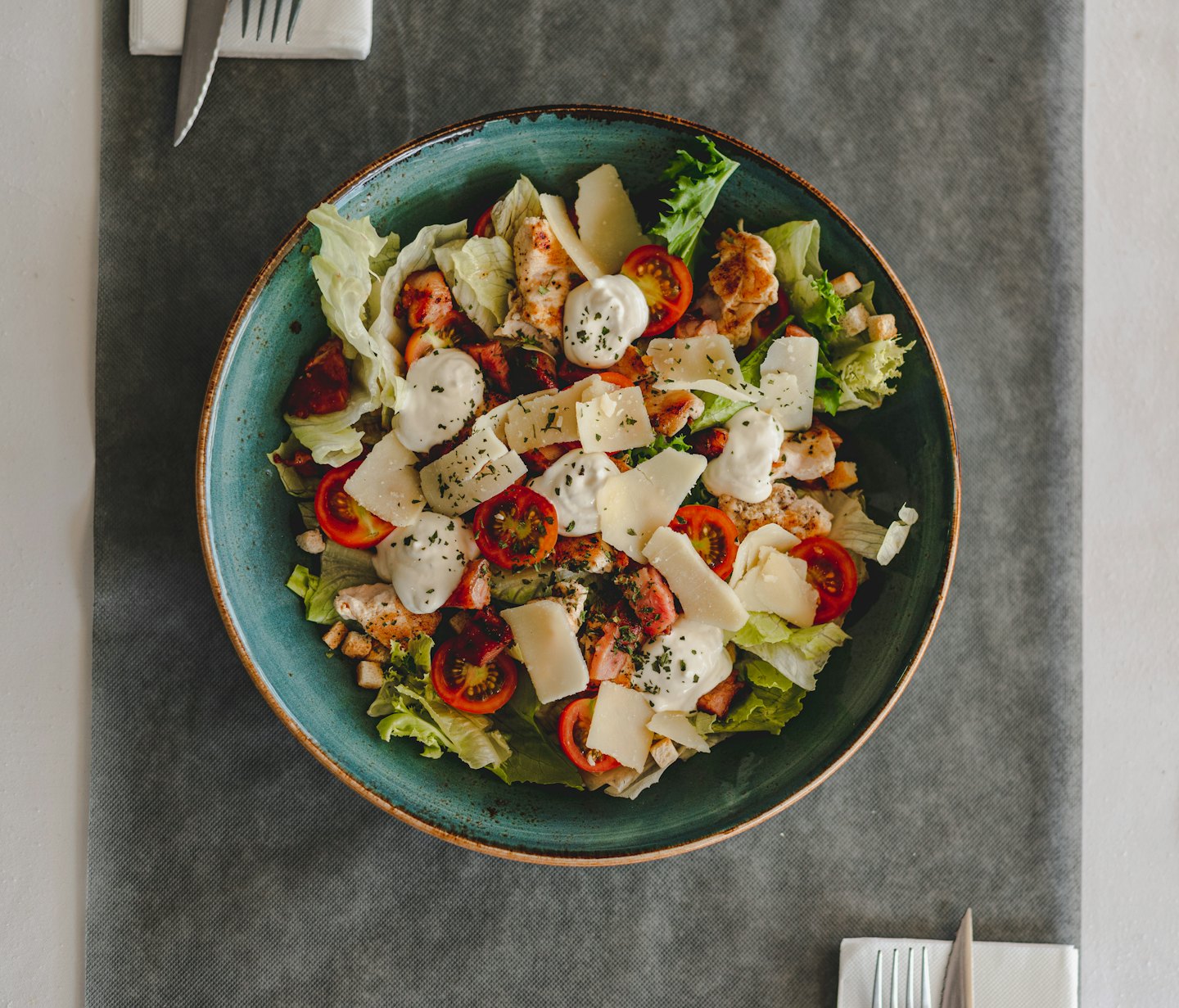 Caesar salad with grilled chicken and cherry tomatoes in a teal bowl.
