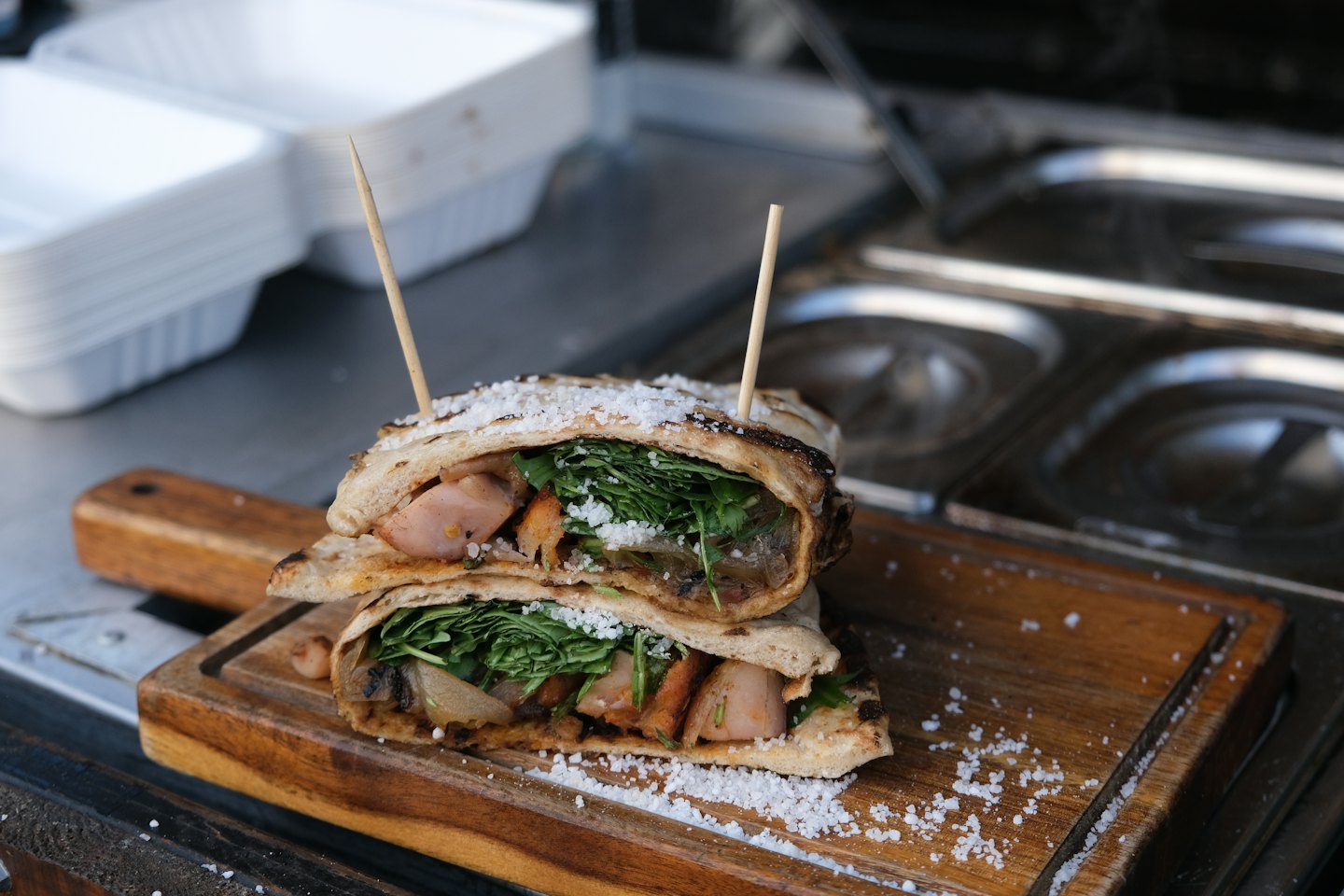 Half wrap sandwich with grilled meat and arugula on wooden board.