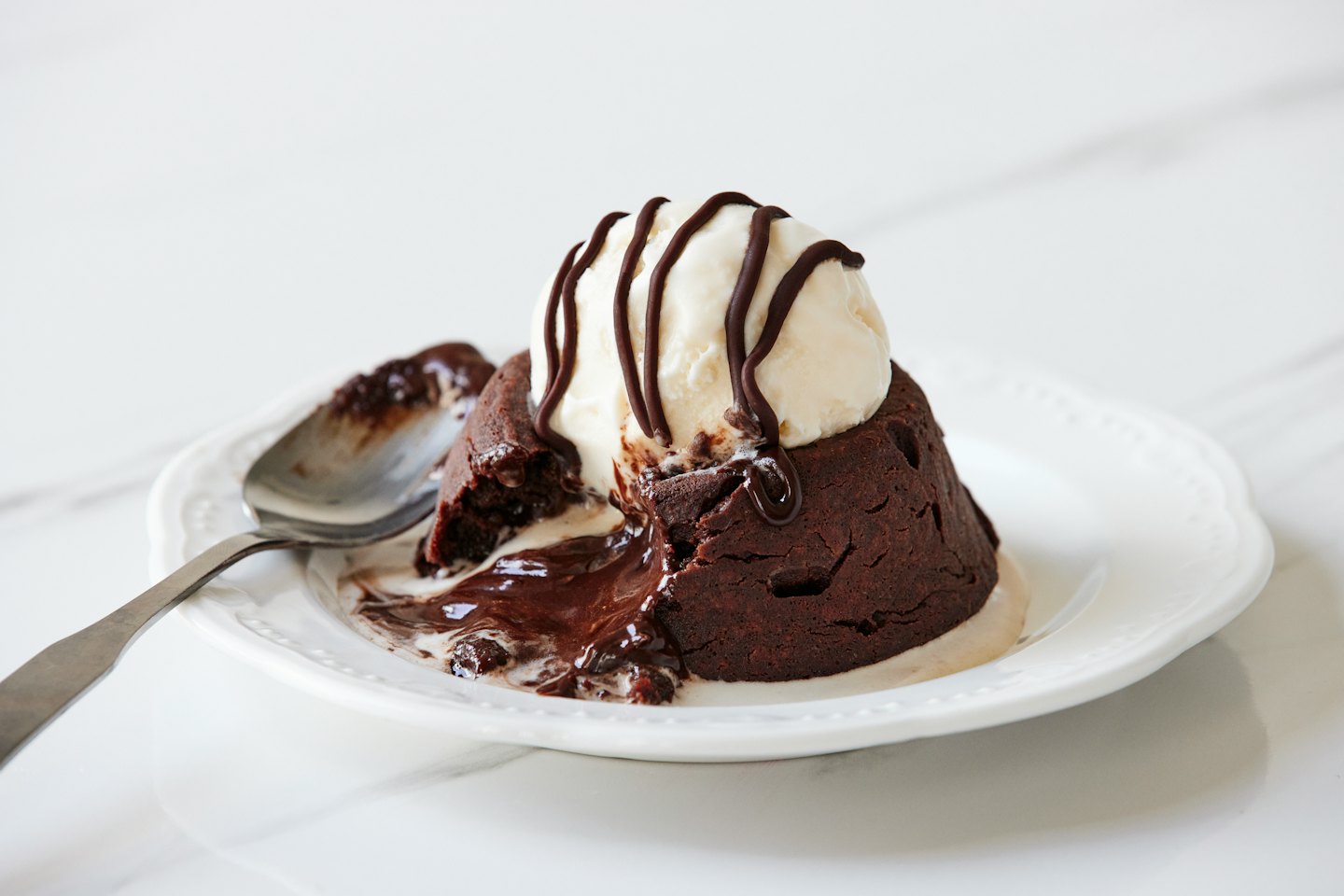 Chocolate lava cake with melting ice cream on a white plate.