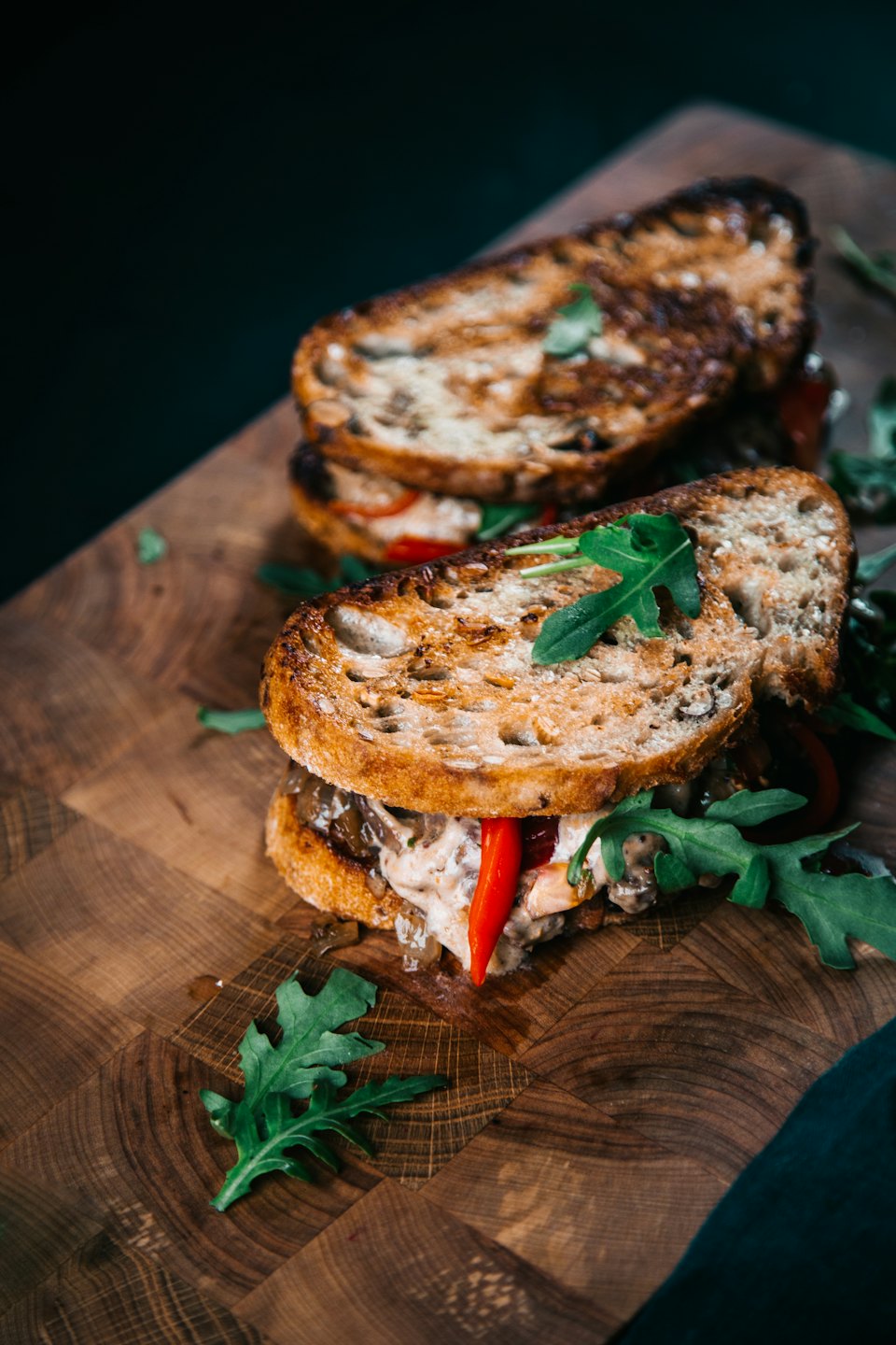 Two gourmet sandwiches on a rustic wooden cutting board.