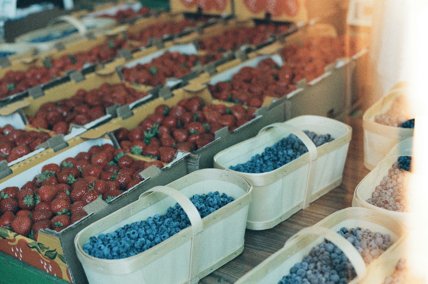 Red strawberries in boxes and blueberries in baskets at a market.