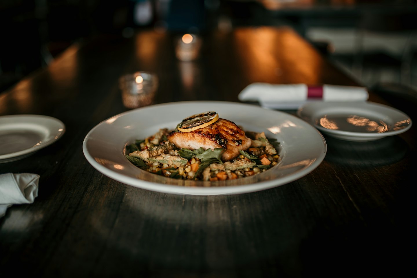 Grilled salmon with lemon and roasted vegetables in a white bowl.
